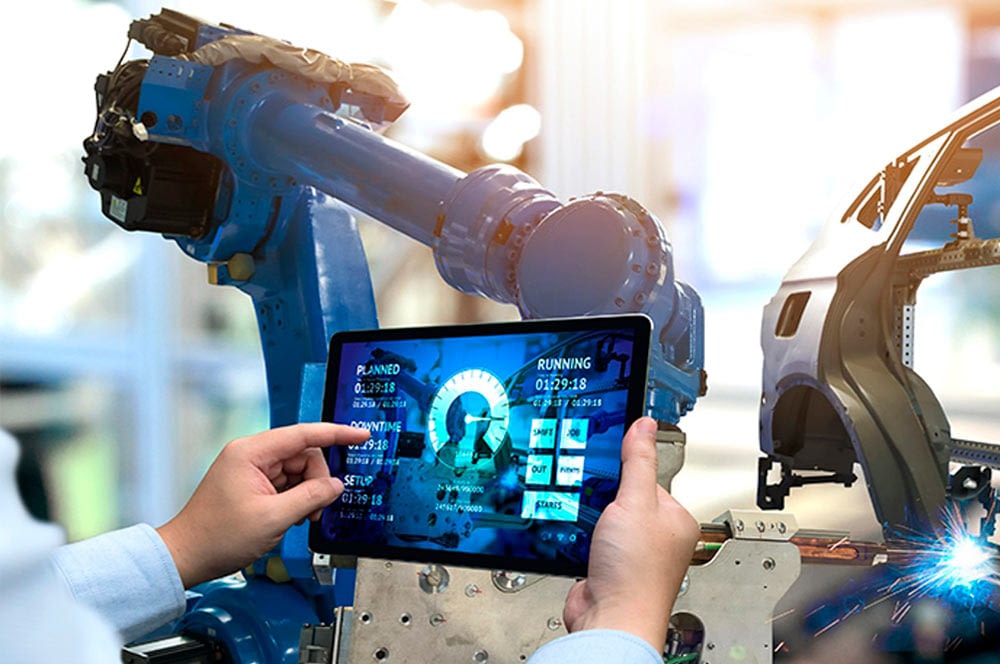  A technician wearing a lab coat uses a tablet to monitor the robotic assembly of an electric vehicle.